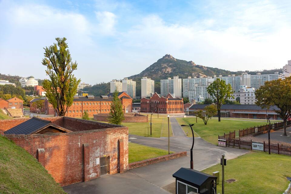 Um campus com edifícios de tijolo, um campo gramado e uma montanha ao fundo.