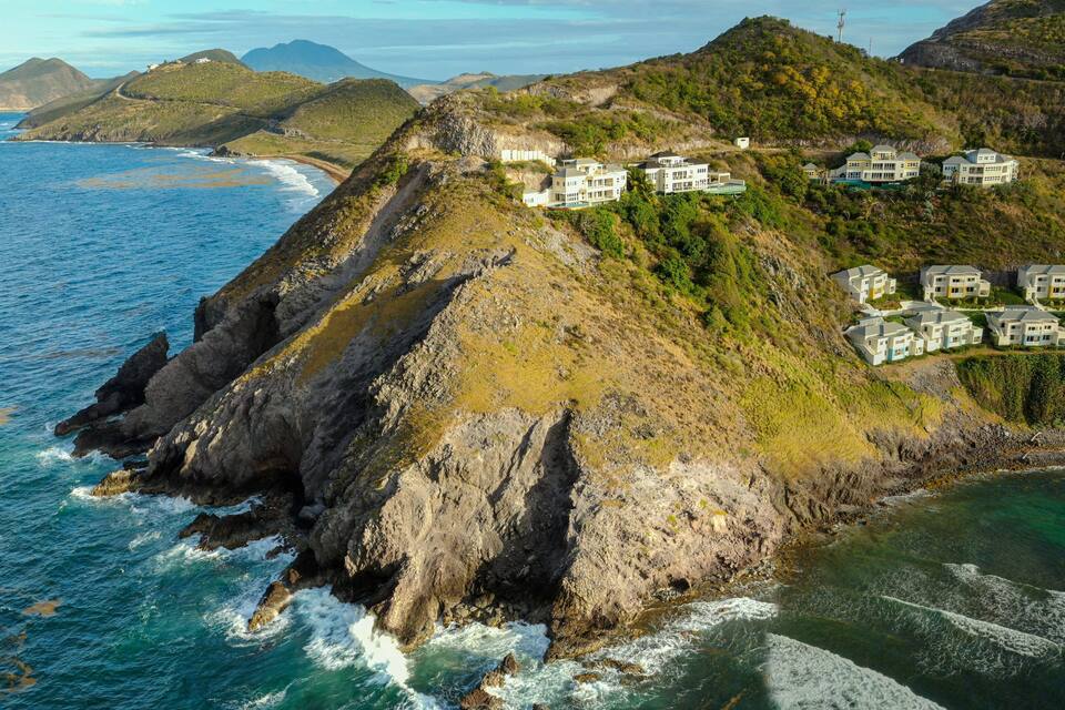 Paisagem costeira com um empreendimento imobiliário à beira de um penhasco, com vista para o oceano.