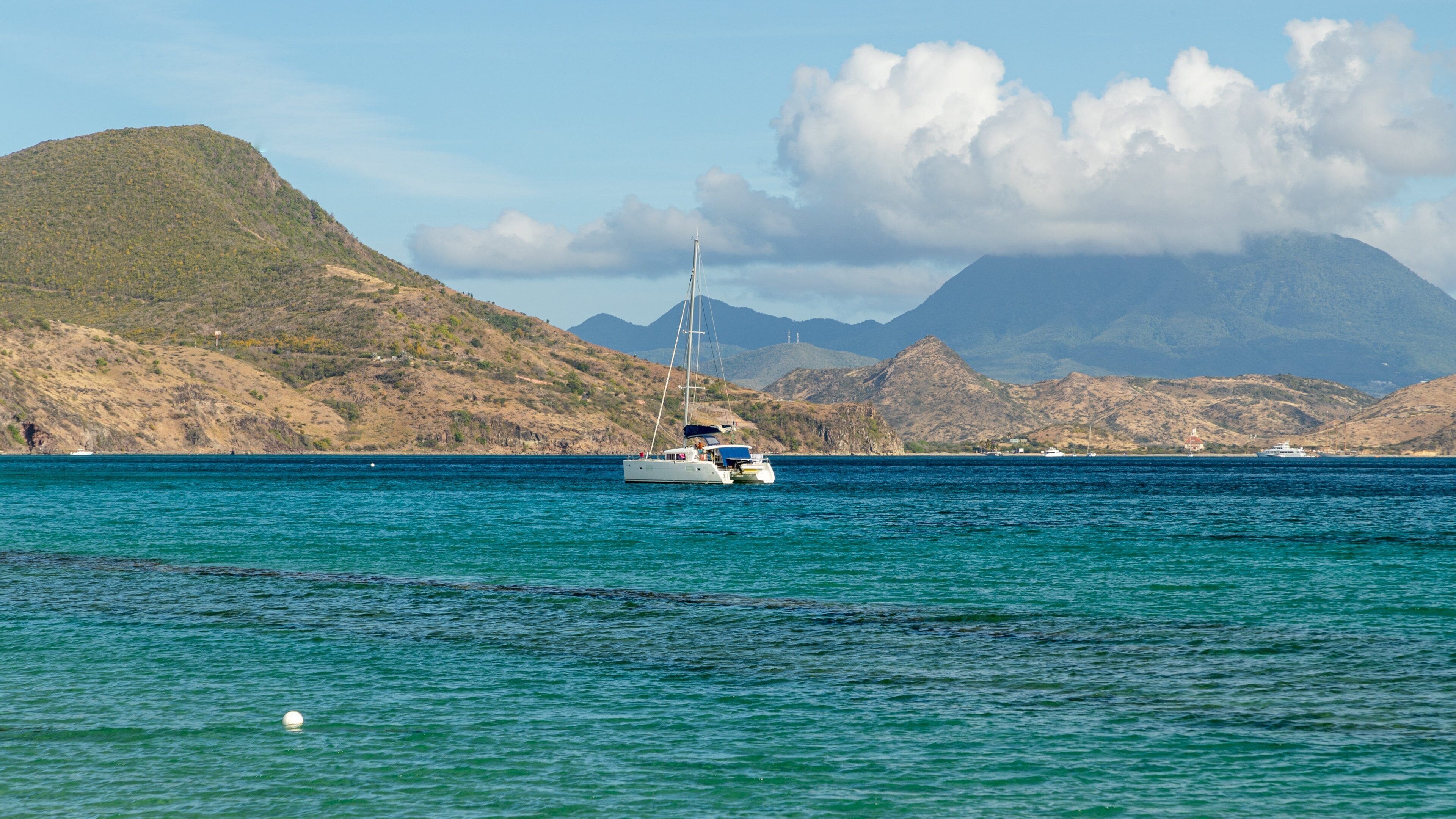 A sailboat on calm turquoise waters with a mountainous backdrop.