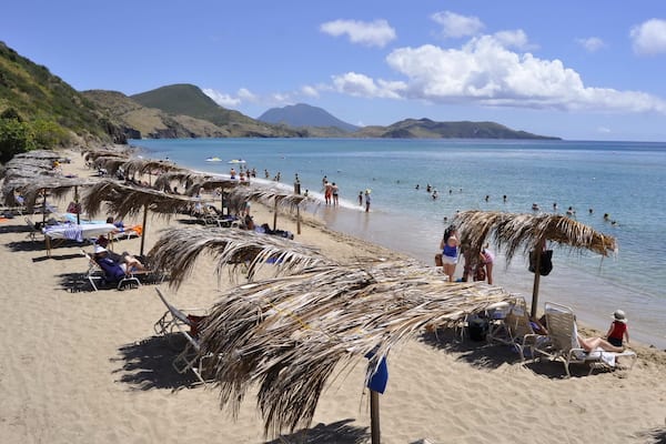 Une plage avec des parasols en chaume, des chaises longues et des gens qui se baignent.