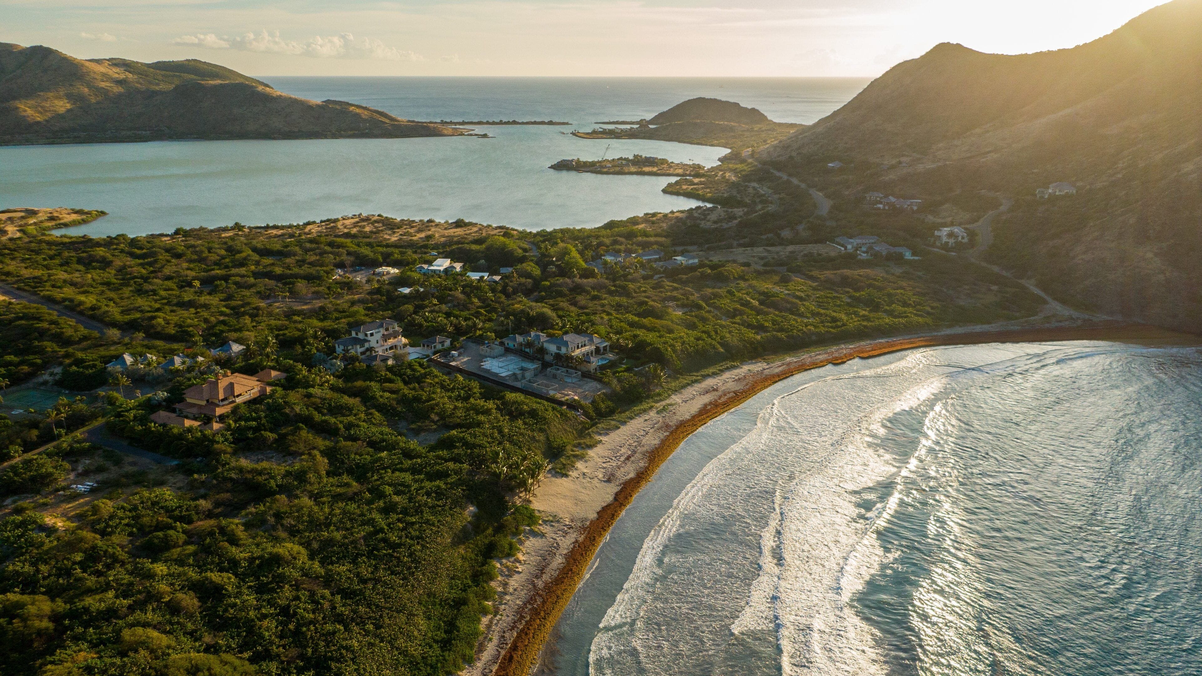 A coastal landscape with a beach, houses, and a bay with islands.
