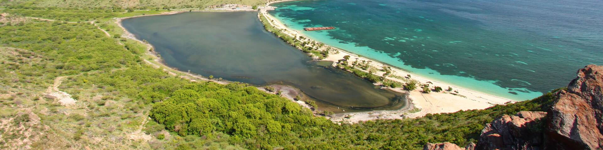 A coastal landscape with a bay, clear waters, and green hills.