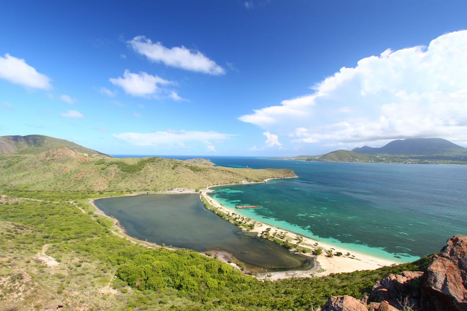 A coastal landscape with a bay, clear waters, and green hills.