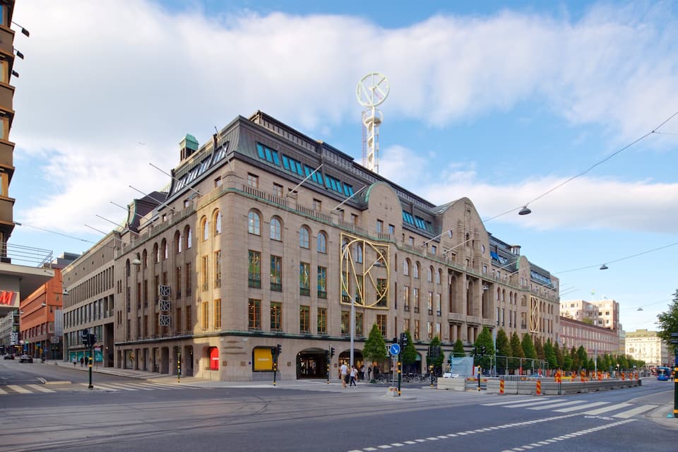 A historic building with a large clock tower, a modern H&M store, and a tram line.