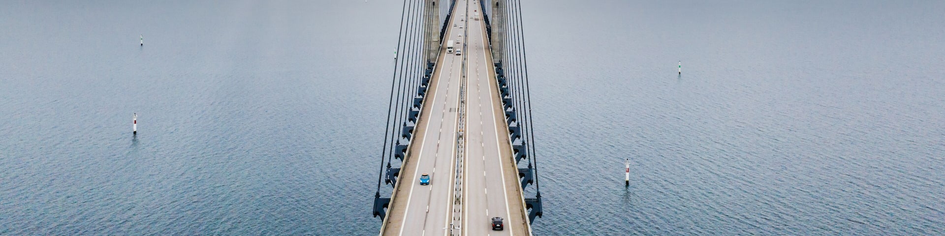 A large suspension bridge spanning a wide body of water with a cloudy sky above.