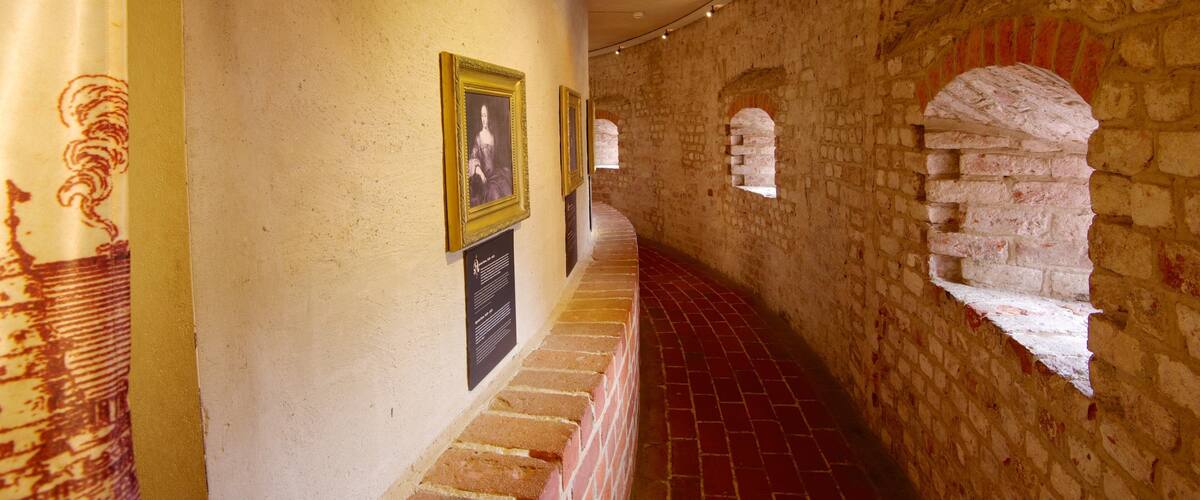 A corridor with stone walls, red brick flooring, and framed pictures on the wall.