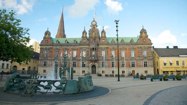 Un edificio histórico con arquitectura ornamentada, una torre destacada y una fuente al frente.