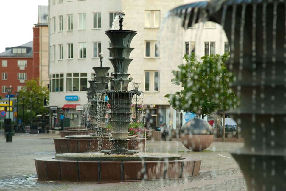 A multi-tiered fountain with water cascading down its tiers, set in a square with buildings in the background.