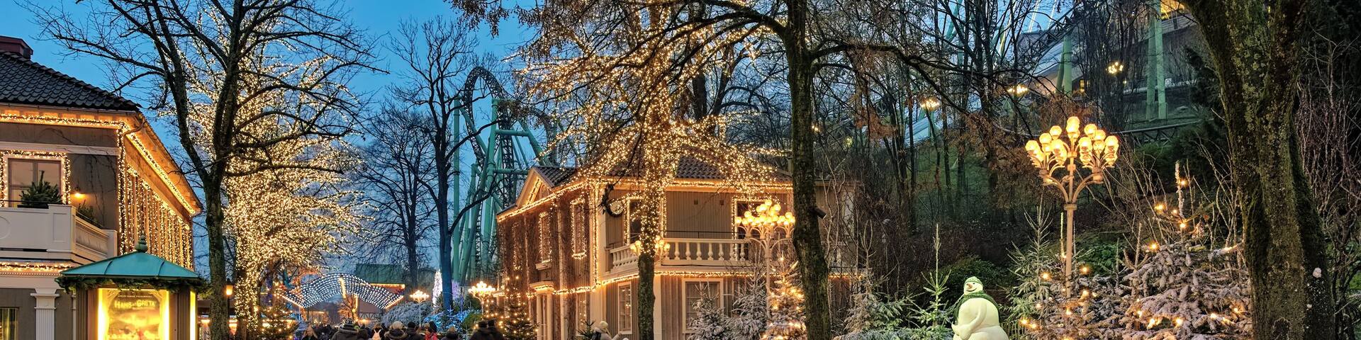 Calle arbolada con edificios iluminados y un árbol de Navidad cubierto de nieve.