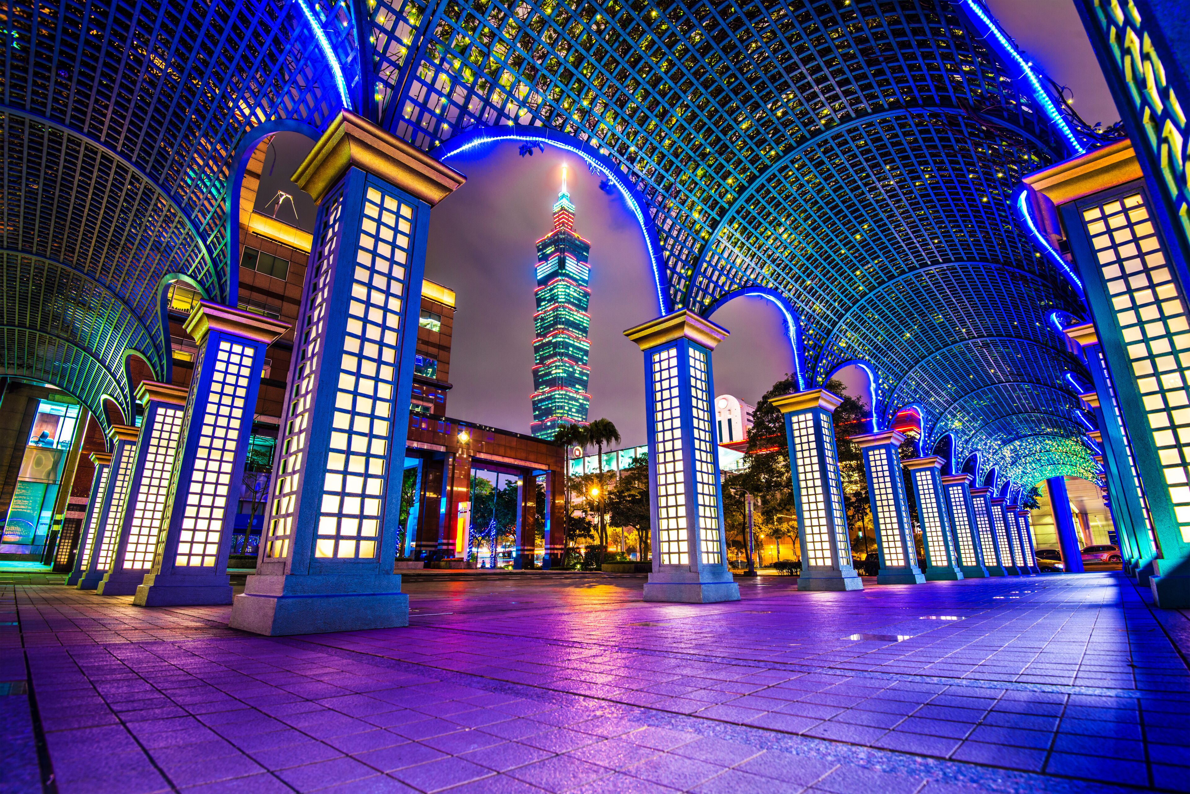 A brightly lit pedestrian area with a prominent tower and a series of illuminated columns.