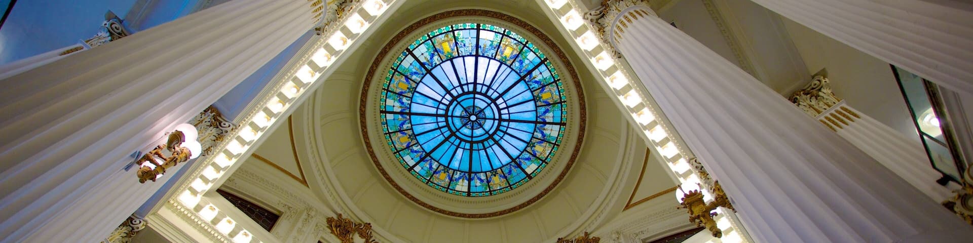 A grand hall with a large circular stained glass window, ornate columns, and a high ceiling.
