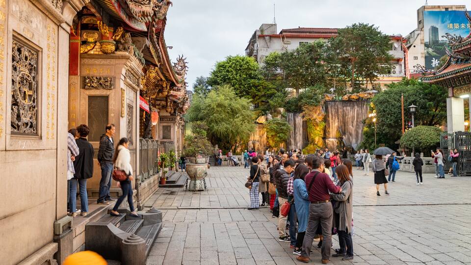 A bustling square with traditional architecture, a prominent fountain, and a crowd of people.