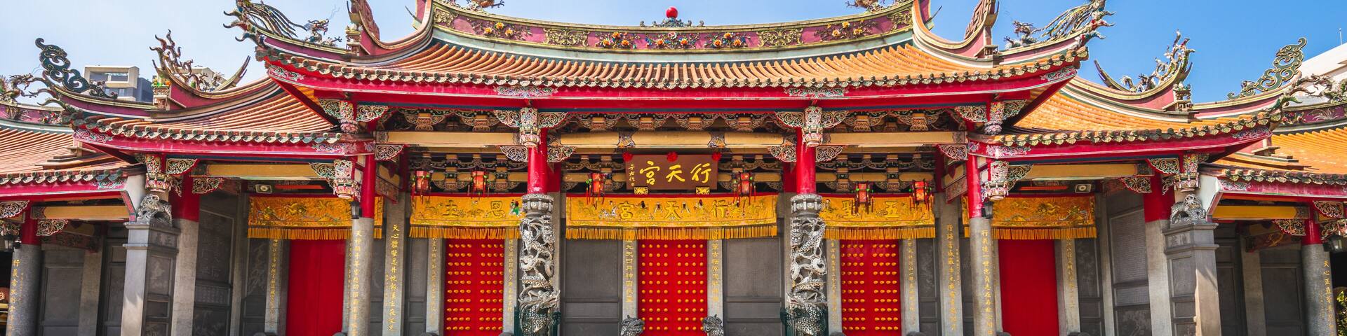 Un templo chino tradicional con techos ornamentados en rojo y dorado, grandes puertas rojas y tallas intrincadas.