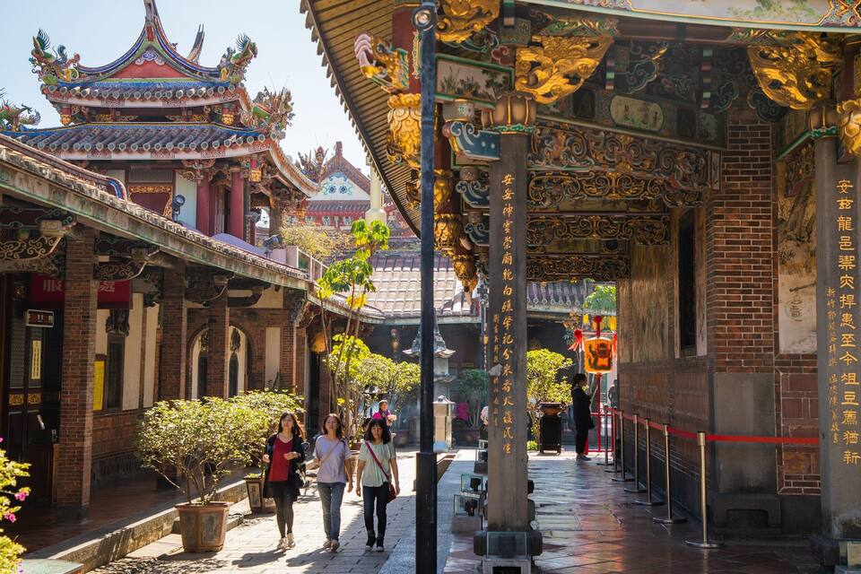Um complexo arquitetônico tradicional chinês com telhados elaborados, paredes de tijolo e um edifício com telhado vermelho e motivos de dragão.