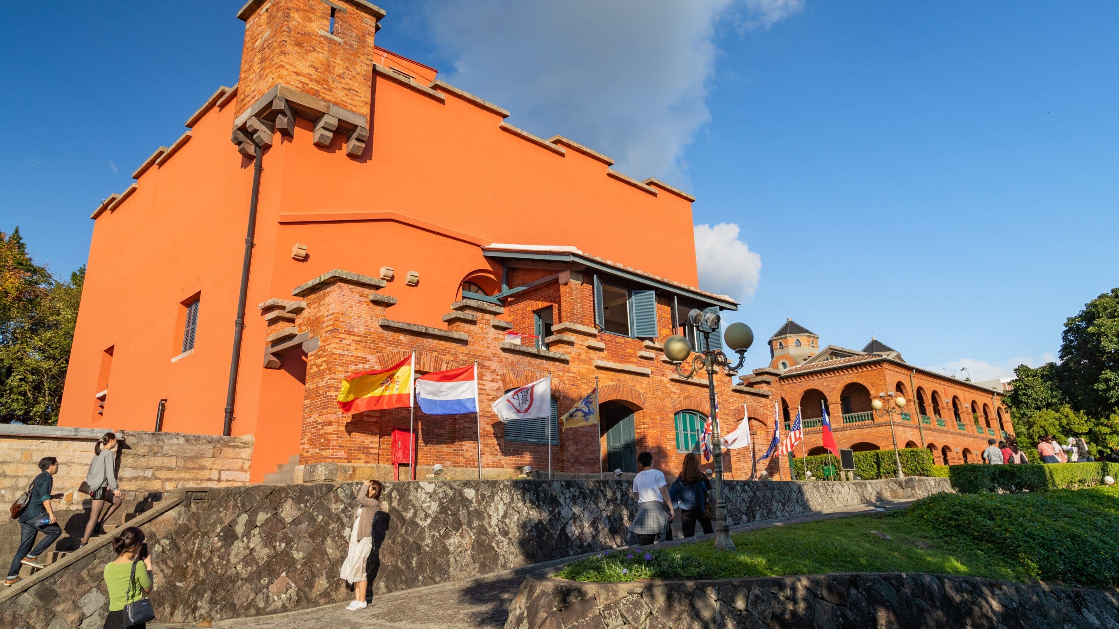 A historic building with a brick facade and a tower, surrounded by flags and visitors.