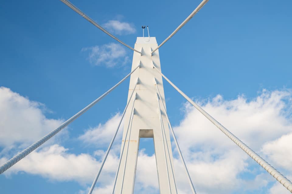 A bridge with a white tower and cables against a blue sky with clouds.