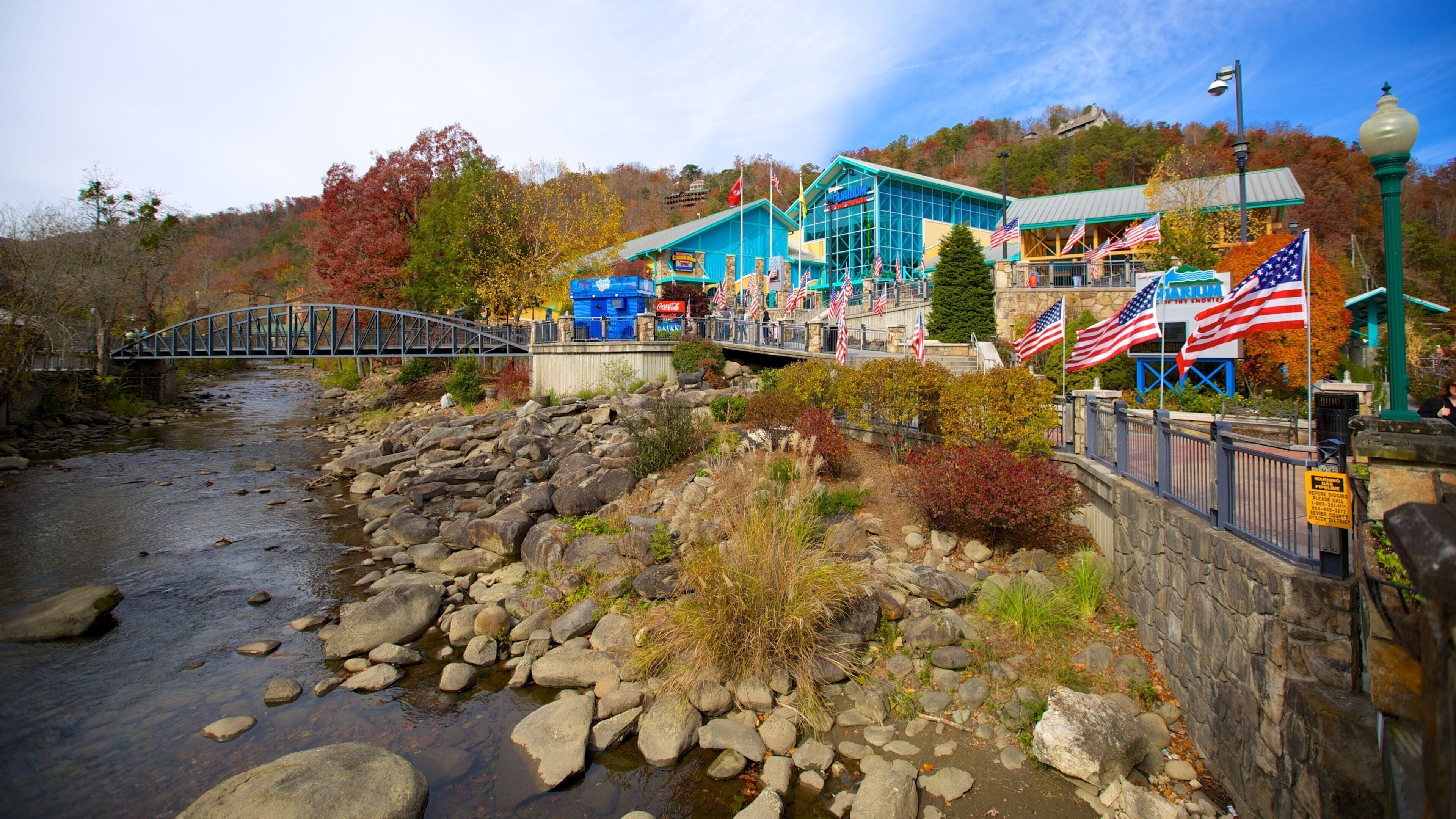 Un río con rocas, un puente, un edificio con banderas estadounidenses y árboles de otoño.