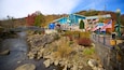 A river with rocks, a bridge, a building with American flags, and autumn trees.