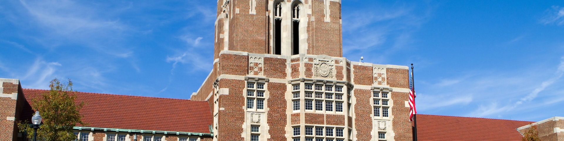 A large brick building with a clock tower, a flag, and a red roof.