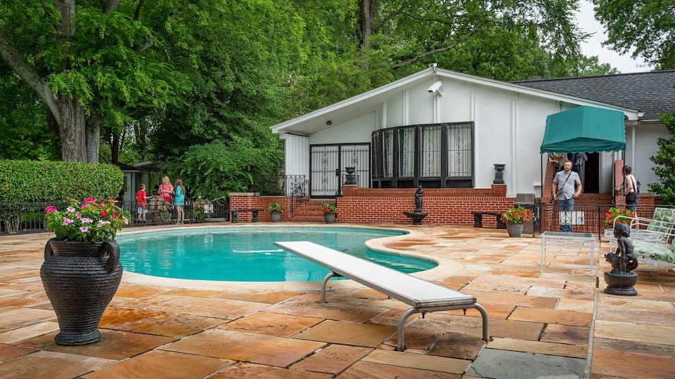 A swimming pool with a white deck, surrounded by a brick patio and potted plants.