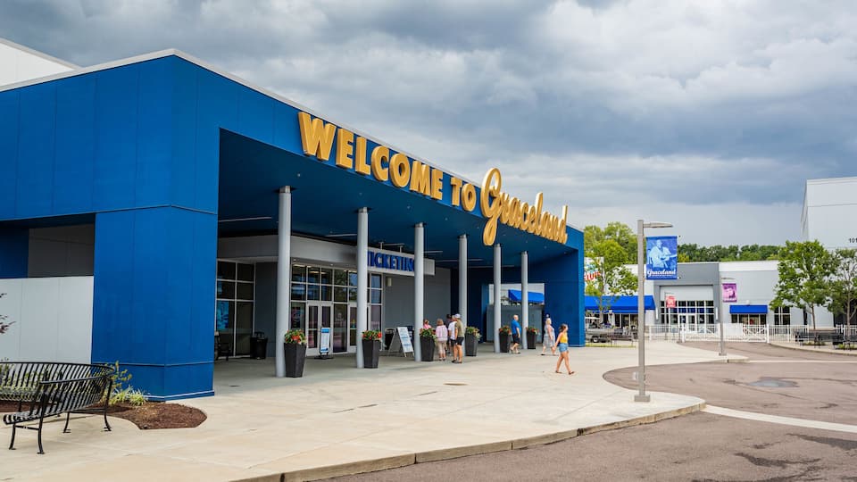 A blue building with a 'Welcome to Graceland' sign, ticketing booth, and people standing outside.