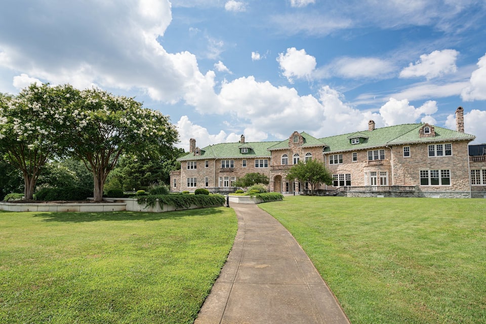 A large stone mansion with a green roof and a well-maintained lawn.