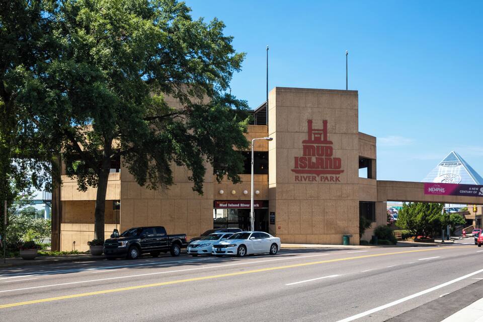 A building with a sign reading "Mud Island River Park" and a parking lot with several cars.