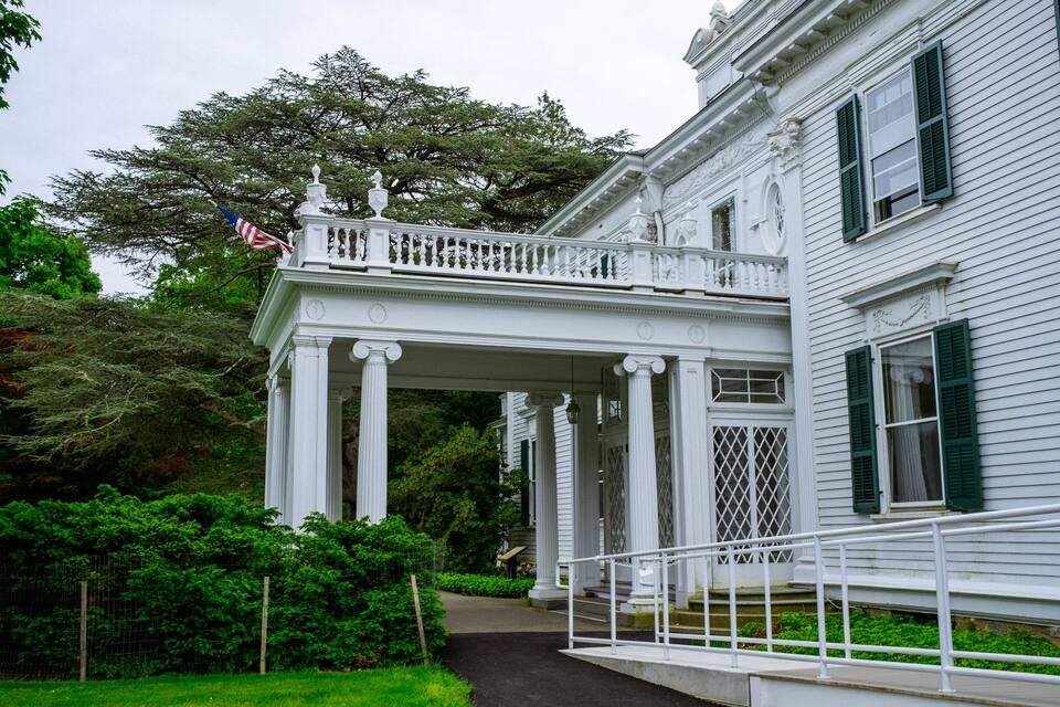 Una casa de estilo colonial blanco con un balcón, contraventanas verdes y una bandera estadounidense.