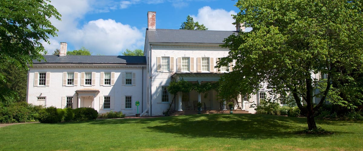 A large white house with a grey roof, surrounded by lush green grass and trees.