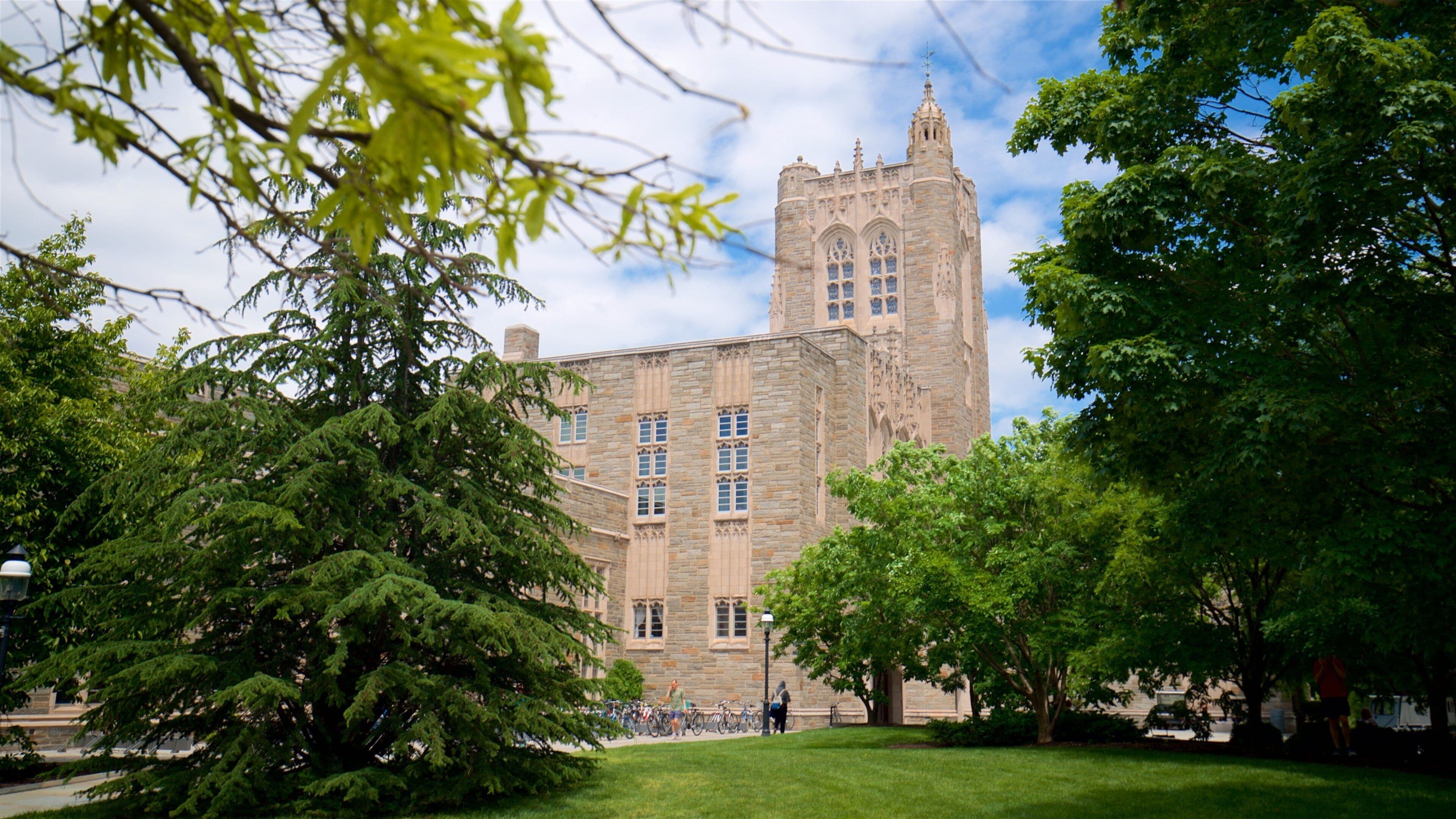 A historic stone building with a tall tower, surrounded by lush green trees and a grassy lawn.