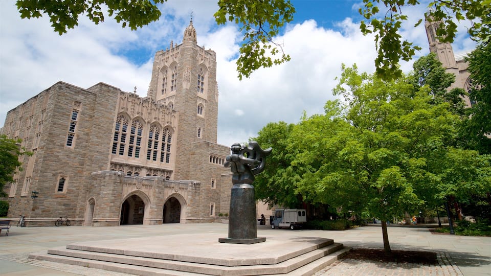 A historic stone building with a clock tower, surrounded by trees and a statue in the foreground.