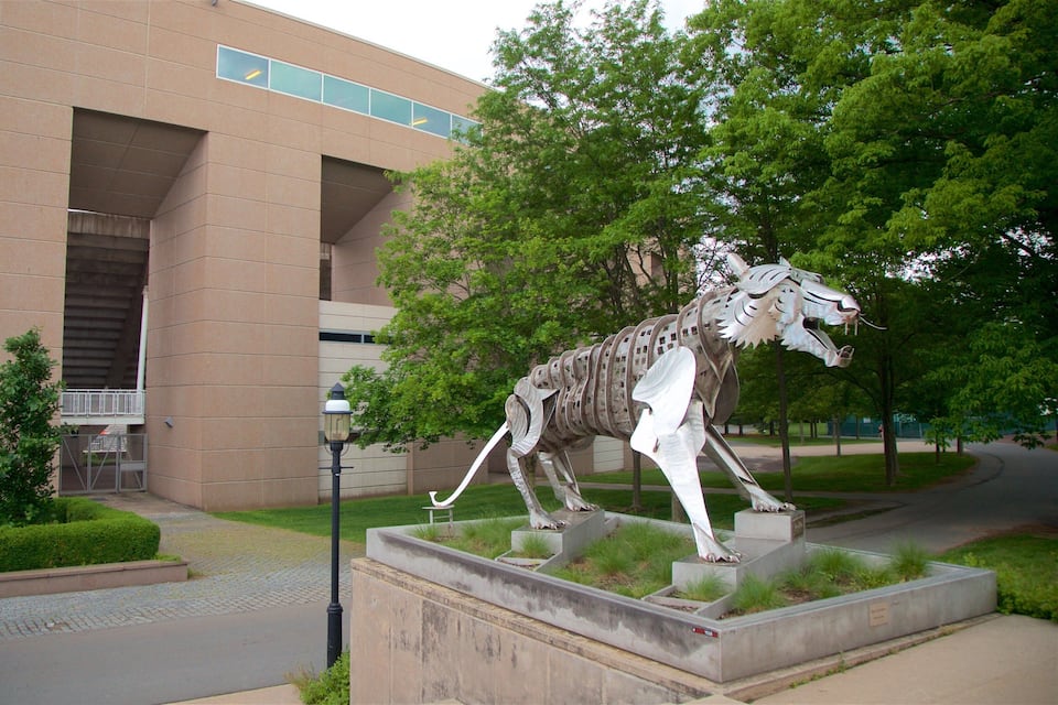 A sculpture of a horse in a landscaped area with a building in the background.