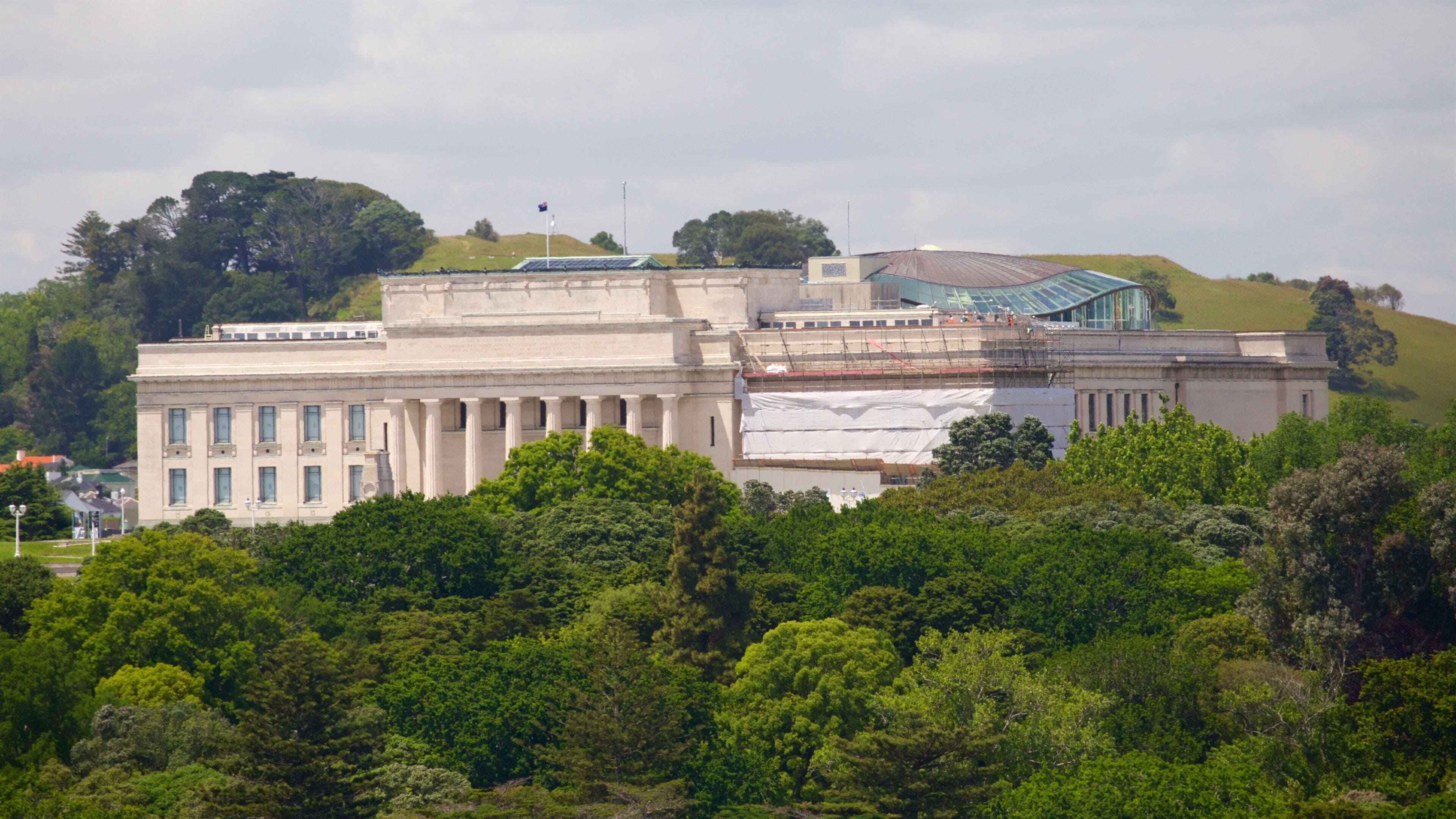 A large classical building with columns, surrounded by lush green trees and hills.