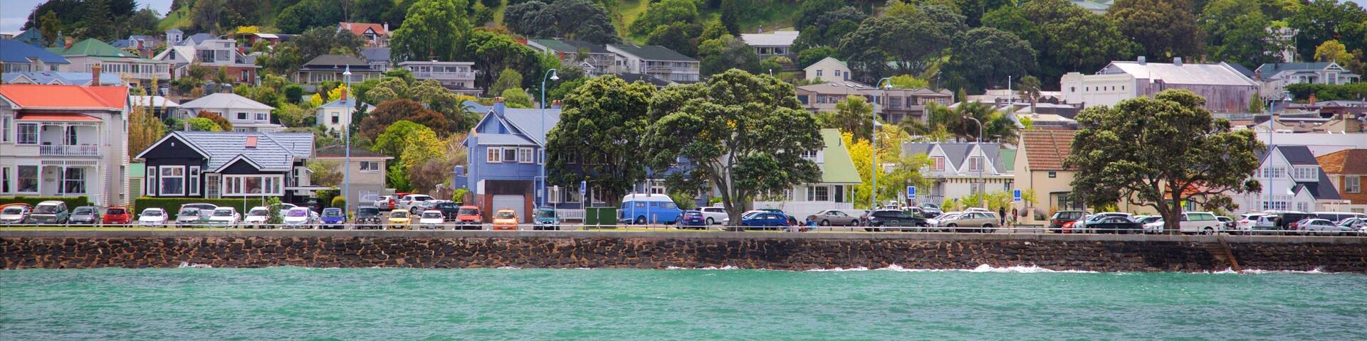 A coastal town with houses, a hill with trees, and a rocky breakwater.