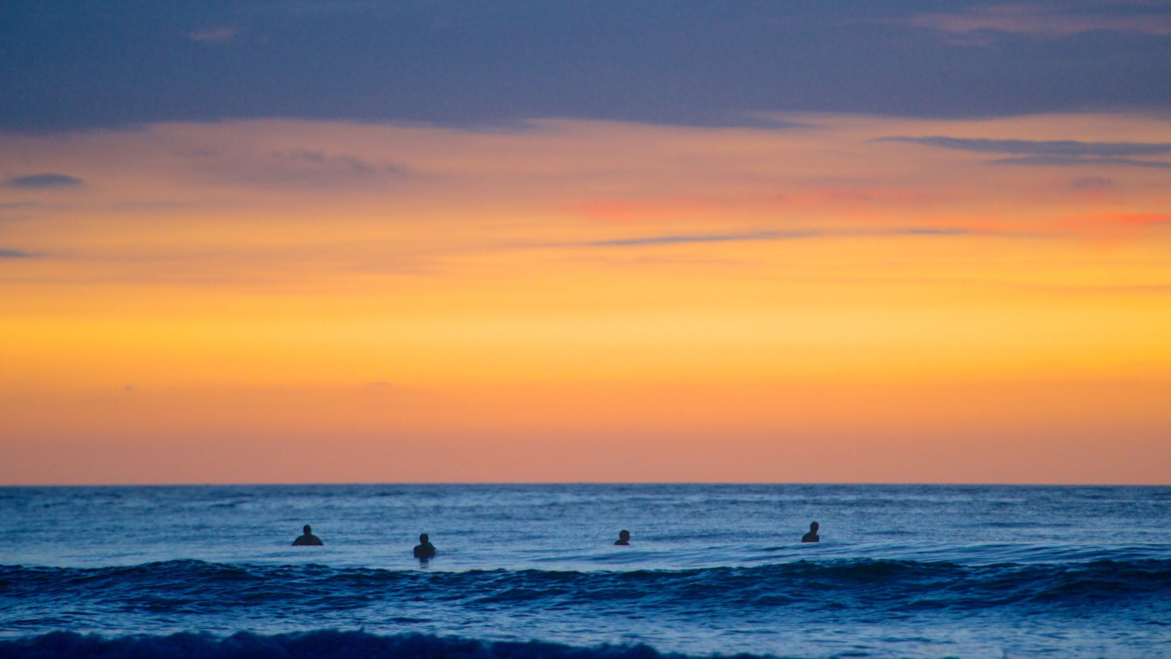 A sunset over the ocean with three people swimming.