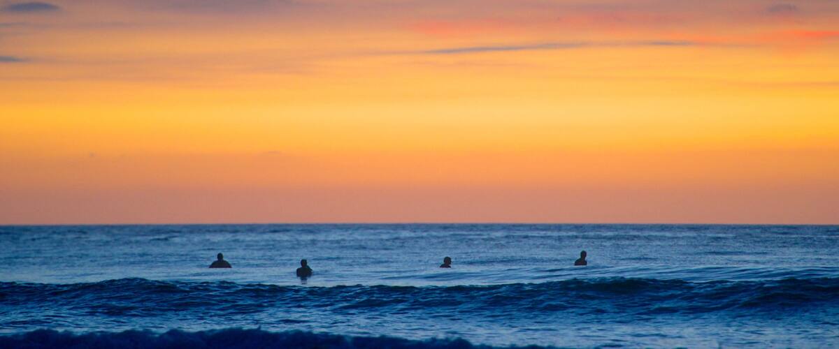 A sunset over the ocean with three people swimming.