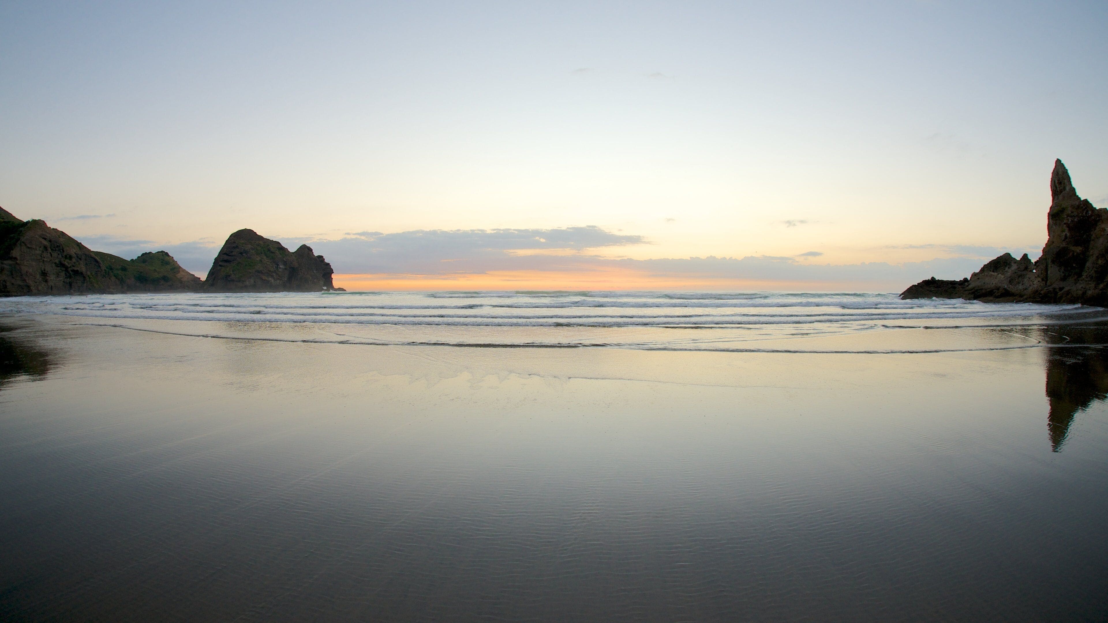 A beach with calm waters, rocky cliffs, and a sunset sky.