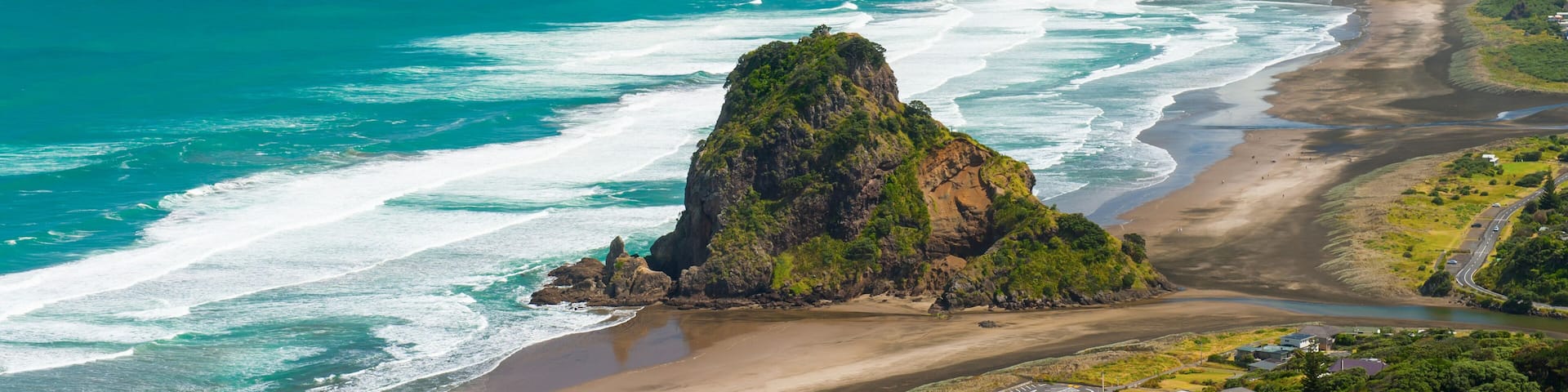 A coastal landscape with a prominent rocky outcrop, a sandy beach, and the ocean.