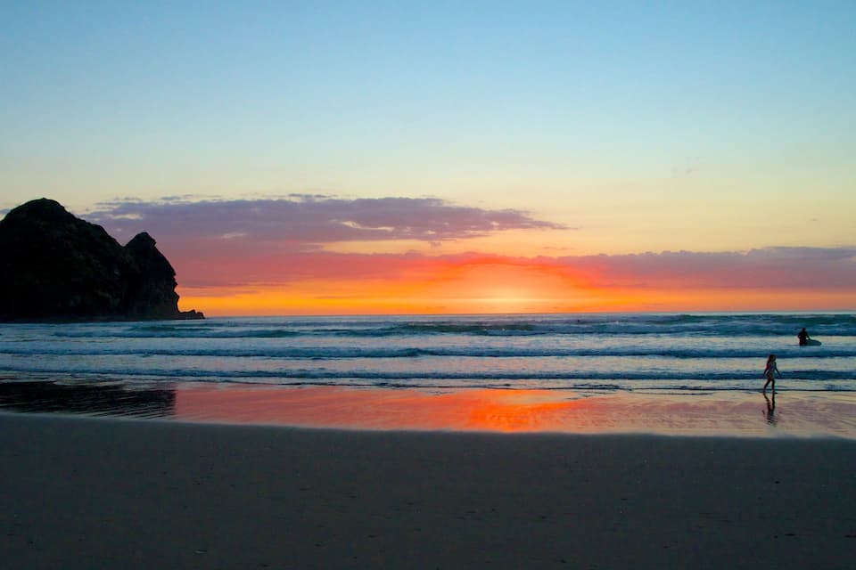 Ein Strand mit Wellen und einer großen Felsformation im Sonnenuntergang.