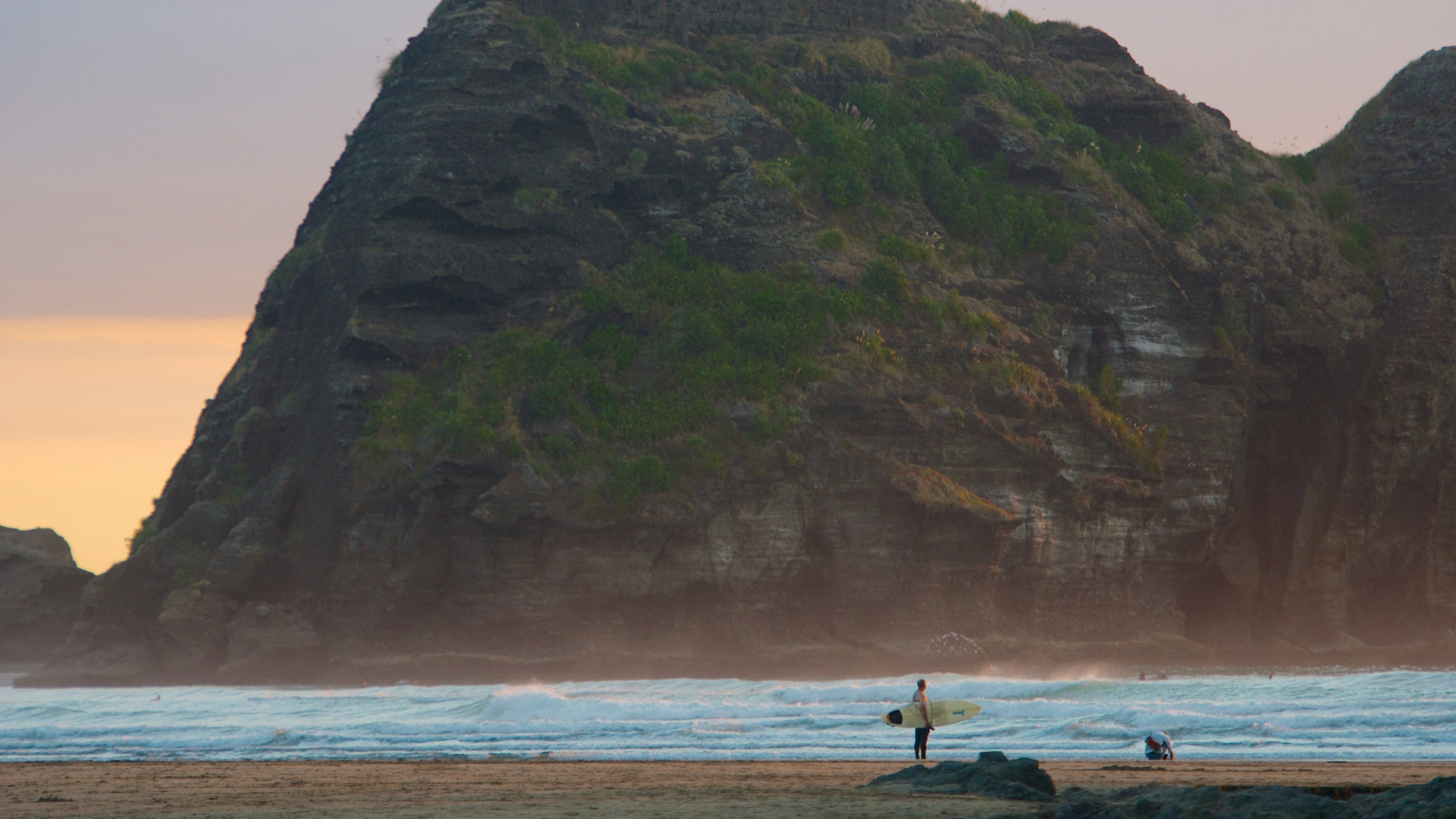 Piha Beach das einen Sandstrand, Sonnenuntergang und Berge