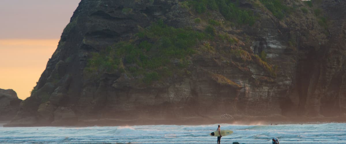 Una playa con una gran formación rocosa y olas rompiendo en la orilla.