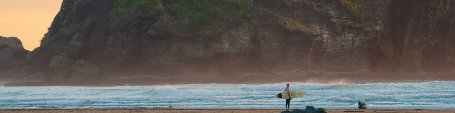 Piha Beach showing mountains, surfing and a sunset