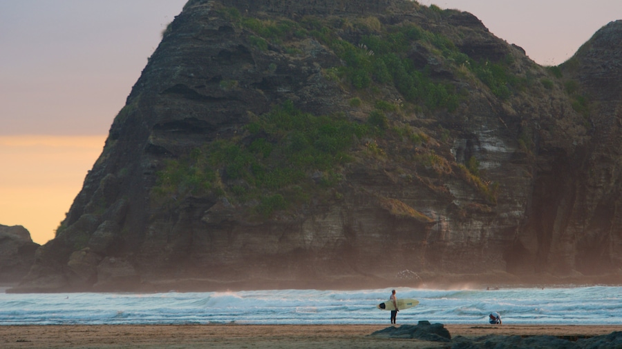 A beach with a large rock formation and waves crashing onto the shore.