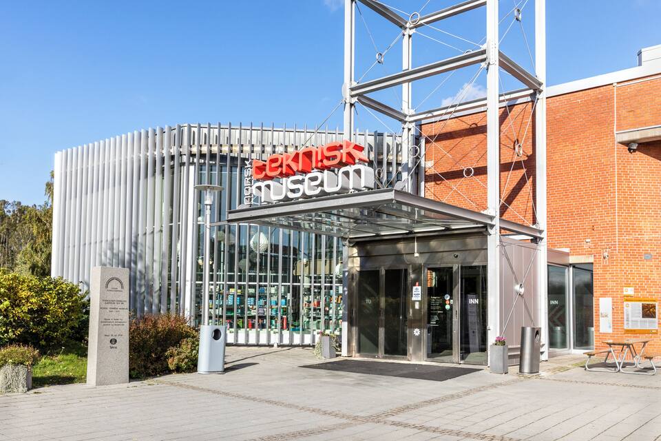 De ingang van het Technische Museum, met een moderne glazen gevel en een rood bord.