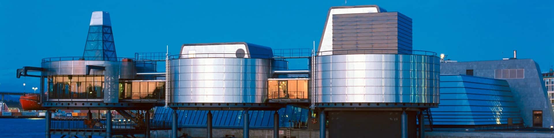 A waterfront industrial complex with large metal storage tanks and a bridge.