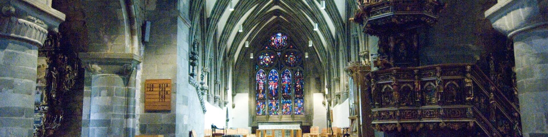 A cathedral interior with Gothic architecture, stained glass windows, and wooden pews.