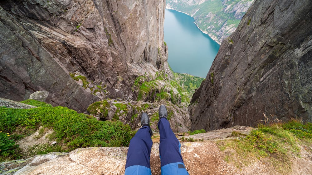 A person standing on a rocky ledge with a view of a deep valley and a lake.