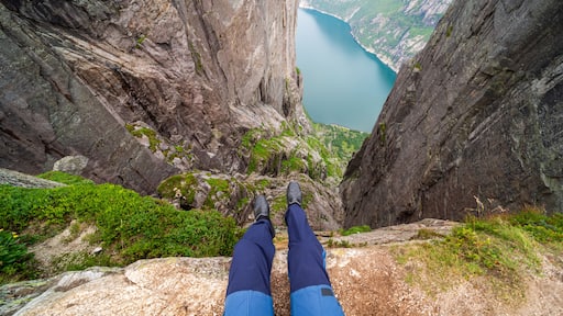 Two feet with hiking boots on them hanging down from a steep cliff with a view on stunning Lysefjorden shimmering with many shades of blue and green. View from Preikestolen. Clear and bright day.