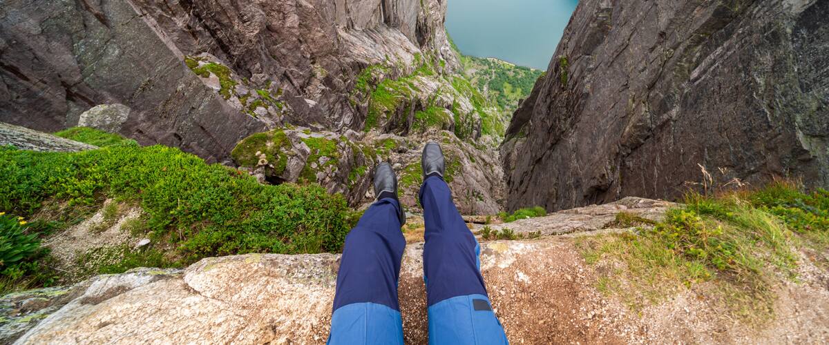 A person standing on a rocky ledge with a view of a deep valley and a lake.