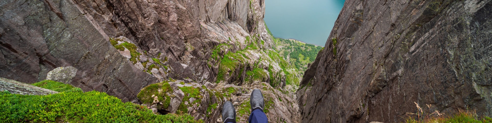 A person standing on a rocky ledge with a view of a deep valley and a lake.